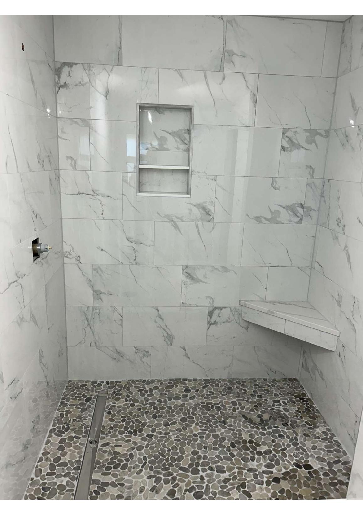 Marble-look tiled shower with pebble accent wall, niche, and bench